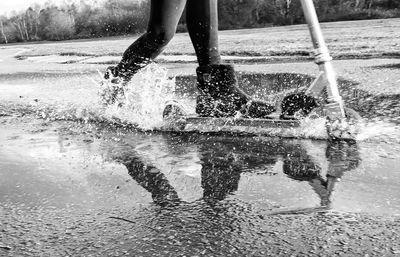 Low section of person riding push scooter on water filled road