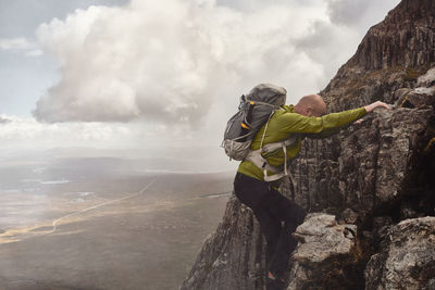 Man climbing a mountain alone above a dramatic landscape. 