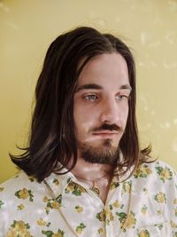 Close-up of young man with long hair looking away against wall