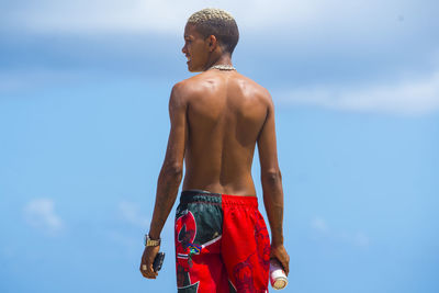 Rear view of shirtless man standing against sky