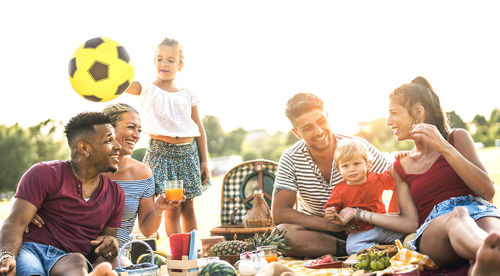 Happy family and friends sitting on field during picnic