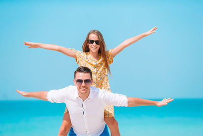 Portrait of smiling young woman with arms raised against sky