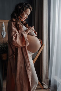 Pregnant woman with mug of hot herbal tea staying in front of window. expecting new baby