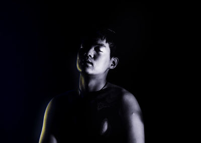 Close-up of shirtless man against black background