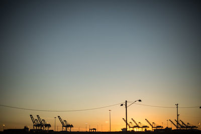 Low angle view of silhouette cranes against clear sky during sunset