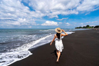 Rear view of woman standing at beach against sky