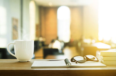 Close-up of coffee cup with diary and eyeglasses on table in cafe