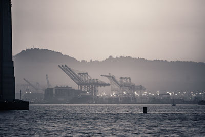 Cranes at harbor against sky