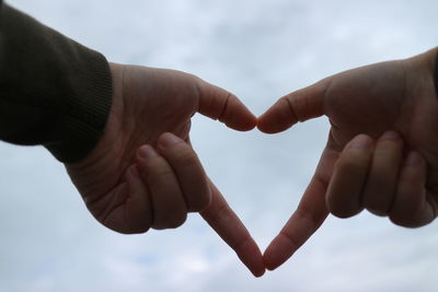 Cropped hands of person making heart shape against sky