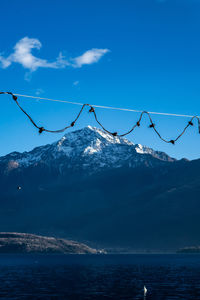 Scenic view of sea by snowcapped mountains against blue sky