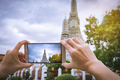 Midsection of woman photographing with mobile phone against sky