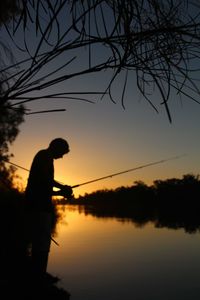 Silhouette man by lake against sky during sunset