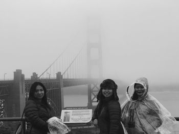 Portrait of smiling young woman against suspension bridge in foggy weather