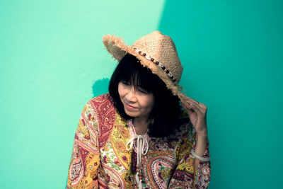 Smiling mature woman wearing hat while against wall