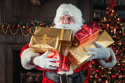 Man wearing santa claus costume holding christmas presents at home