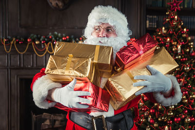 Santa clause holding gift by christmas tree at home