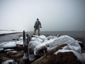 Rear view of man standing on snow covered sea shore against sky