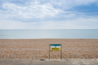 Information sign on beach against sky