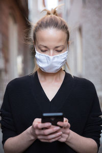 Woman wearing mask using smart phone standing outdoors