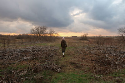 Rear view of woman walking on field against sky