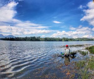 Man sitting on lake against sky