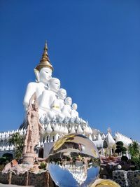 Low angle view of statue by building against clear blue sky