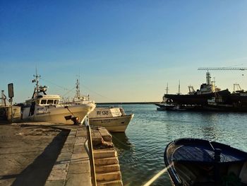 Boats moored at harbor against clear blue sky