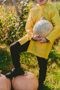 Boy in a yellow raincoat holds a large pumpkin in his hands on the street. preparing for halloween.