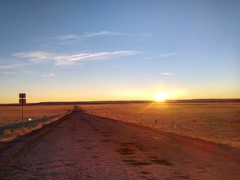 Road amidst field against sky during sunset