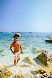 Shirtless man looking away while standing at beach