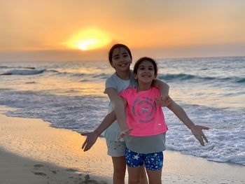 Portrait of two young girls standing hugging at beach during sunset