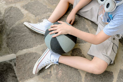 Low section of boy with ball sitting on footpath