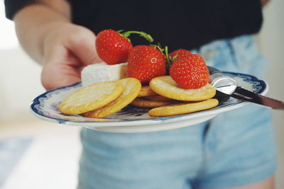 Midsection of woman holding biscuits with strawberries and cheese in plate