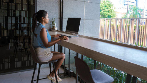 Side view of woman using laptop while sitting on table