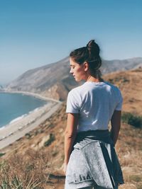 Young woman sitting on shore against clear sky