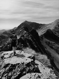 Rear view of hiker walking on mountain against sky