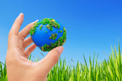 Close-up of hand holding grass against blue sky