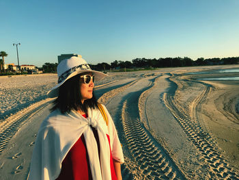 Woman wearing hat while standing at beach against clear blue sky