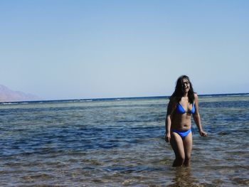 Full length of young woman standing in sea against clear sky