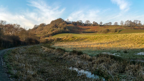 Scenic view of fields, hill and canal against sky