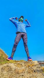 Low angle view of person standing on rock against clear blue sky