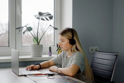 Teenage girl in headphones typing something on her laptop while having online lesson at home