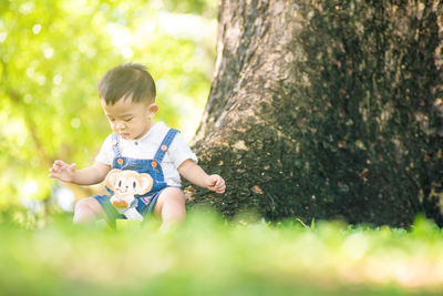 Cute boy sitting on grass against trees