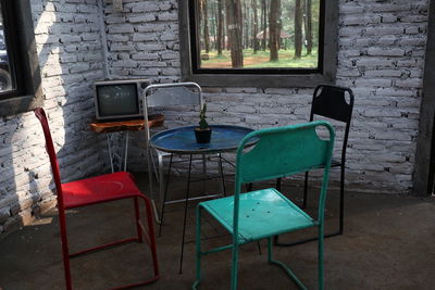 Empty chairs and table against window on wall