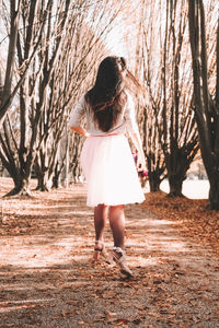 Full length rear view of woman walking on bare tree