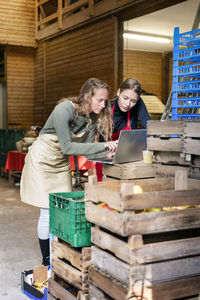 Two women using laptop between crates on a farm