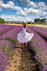 Happy young woman playing with her white dress in the middle of a blooming lavender field. 
