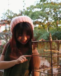 Smiling young woman looking at birdcage while standing in balcony