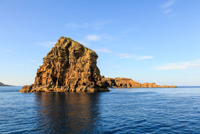 Rock formation by sea against blue sky