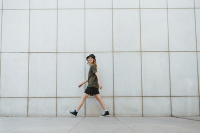 Portrait of young woman walking against wall